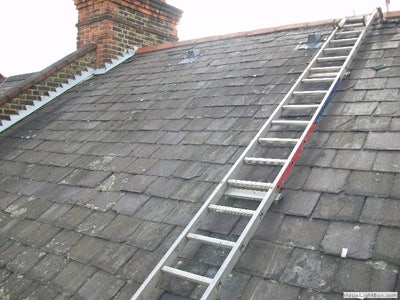 A ladder held in place with roof hooks on a slate roof during maintenance