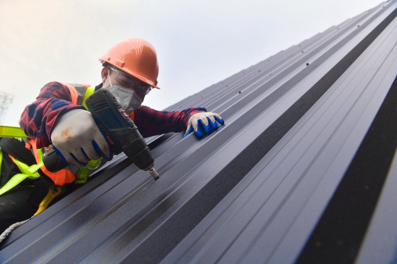 worker securing down metal roof with screws