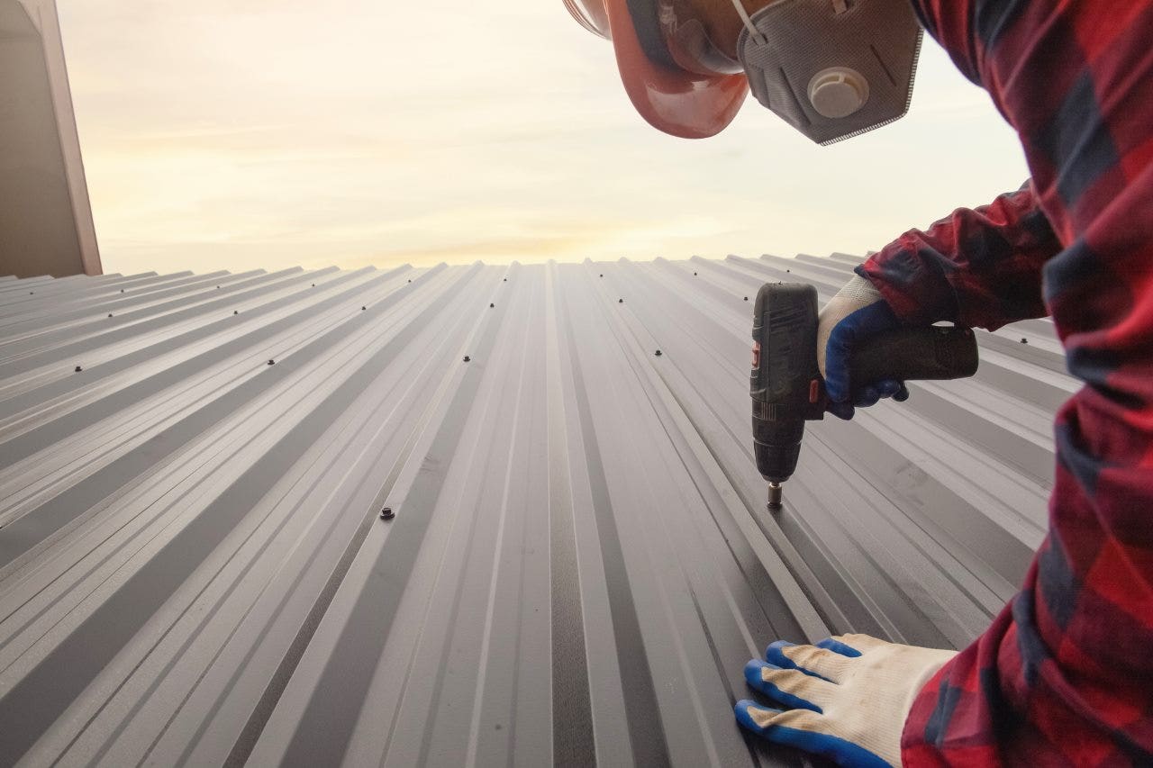 a worker applying screws on a metal roof sheet
